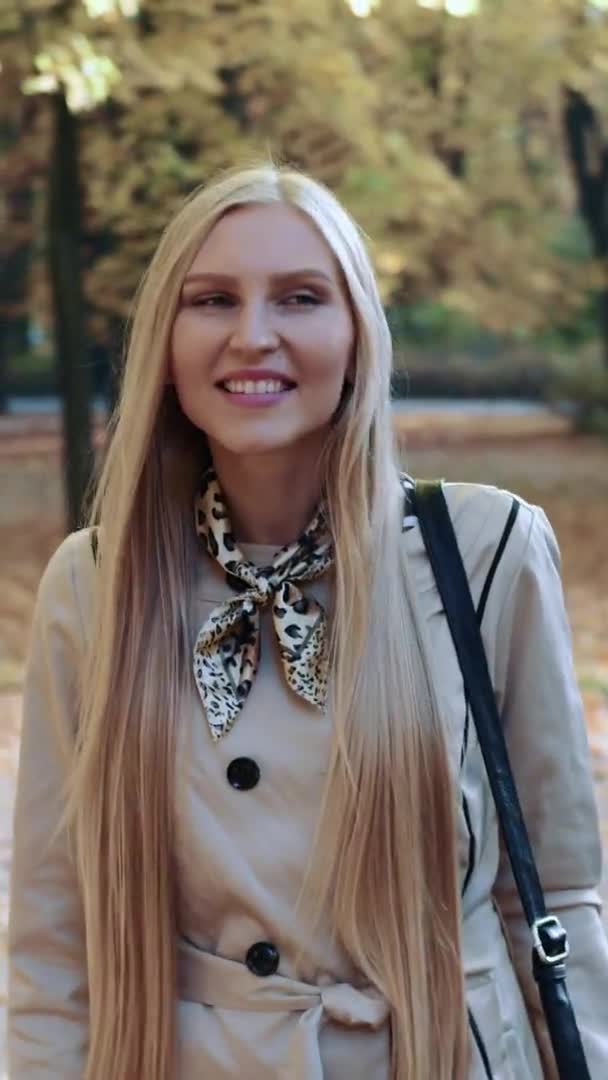 Beautiful young blonde girl walking in the park in autumn and smiling — Stock Video