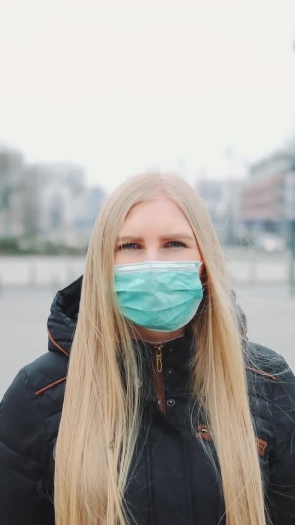 Coronavirus pandemi: blond kvinna i en medicinsk mask går ner på gatan — Stockvideo