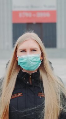 Sokakta yürürken orta boy bir tıbbi maske takan sarışın kadın resmi.