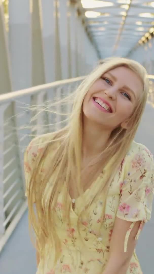 Девушка оглядывается на мост. Красивая блондинка смотрит в камеру, когда бегает по мосту с волнистыми волосами . — стоковое видео
