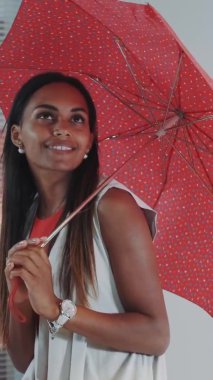 Moda dergisi fotoğraf çekimi için kırmızı şemsiyeli gülümseyen siyah modelin yakın çekimi.