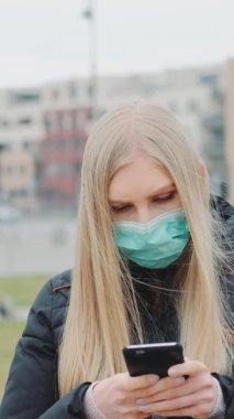 Tıbbi maske takan kadın sokaklarda koronavirüs hastalığı ile ilgili son dakika haberleri okuyor.