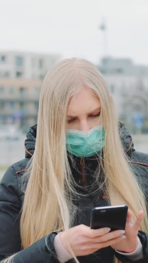 Μέτριο πλάνο του κοριτσιού που φοράει ιατρική μάσκα διαβάζοντας έκτακτα νέα για τη νόσο του Coronavirus στο δρόμο. — Αρχείο Βίντεο
