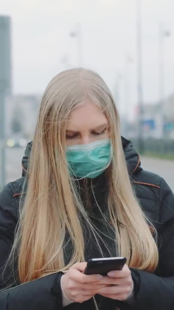 Пандемия коронавируса: блондинка в медицинской маске пишет сообщение на смартфоне — стоковое видео