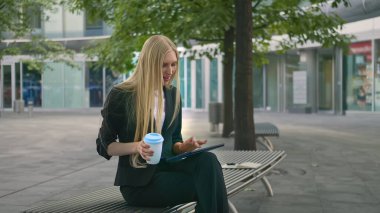 Genç iş kadını tablet kullanıyor ve kahve içiyor. Takım elbiseli modern yönetici kız açık hava sörf tabletinde oturup bir fincan kahve içiyor..