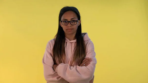 Multiethnic young woman looking over her glasses on yellow background. — Stock Photo, Image