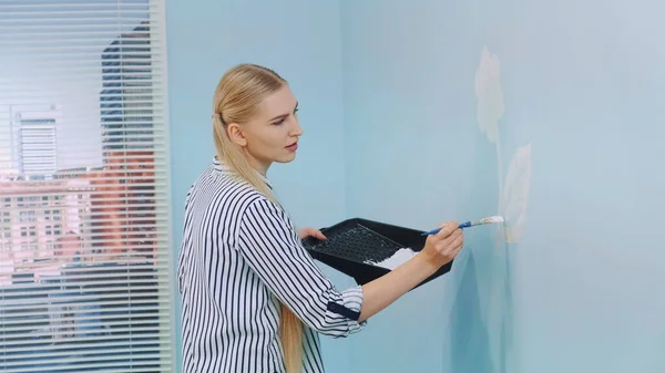 Mujer dibujando una flor en una pared azul — Foto de Stock