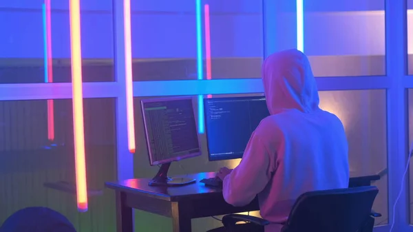 Back view of Hacker in white hoodie penetrating network system in neon room — Stock Photo, Image