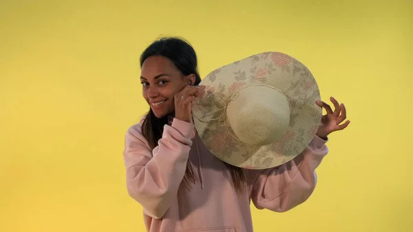 Smiling african woman hiding behind the hat on yellow background. — Stock Photo, Image