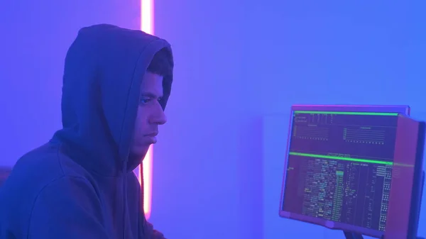 Profile view of african hacker in hoodie working in room filled with display screens — Stock Fotó