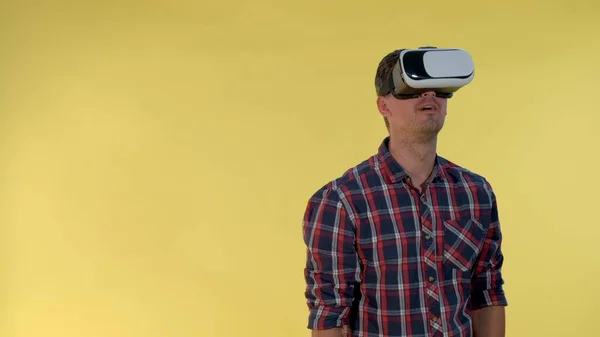 Homem de cabelos escuros usando óculos de realidade virtual enquanto está de pé contra fundo amarelo . — Fotografia de Stock