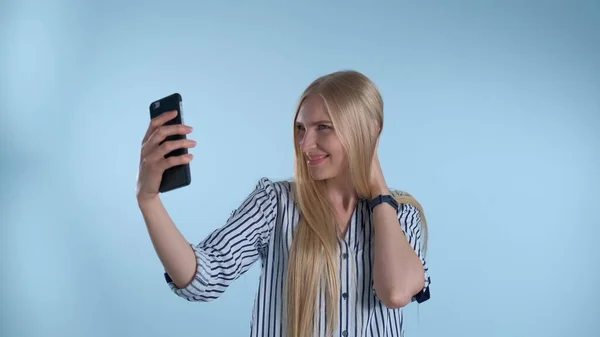 Приваблива блондинка робить селфі на смартфоні на синьому фоні — стокове фото
