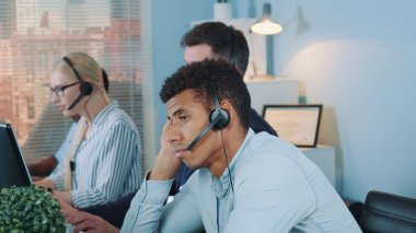 Sıkılmış çok ırklı müşteri destek operatörü müşteriden telefon bekliyor.