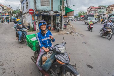 Gülümseyen Vietnamlı bir kadın motosiklet sürüyor ve kameraya bakıyor..
