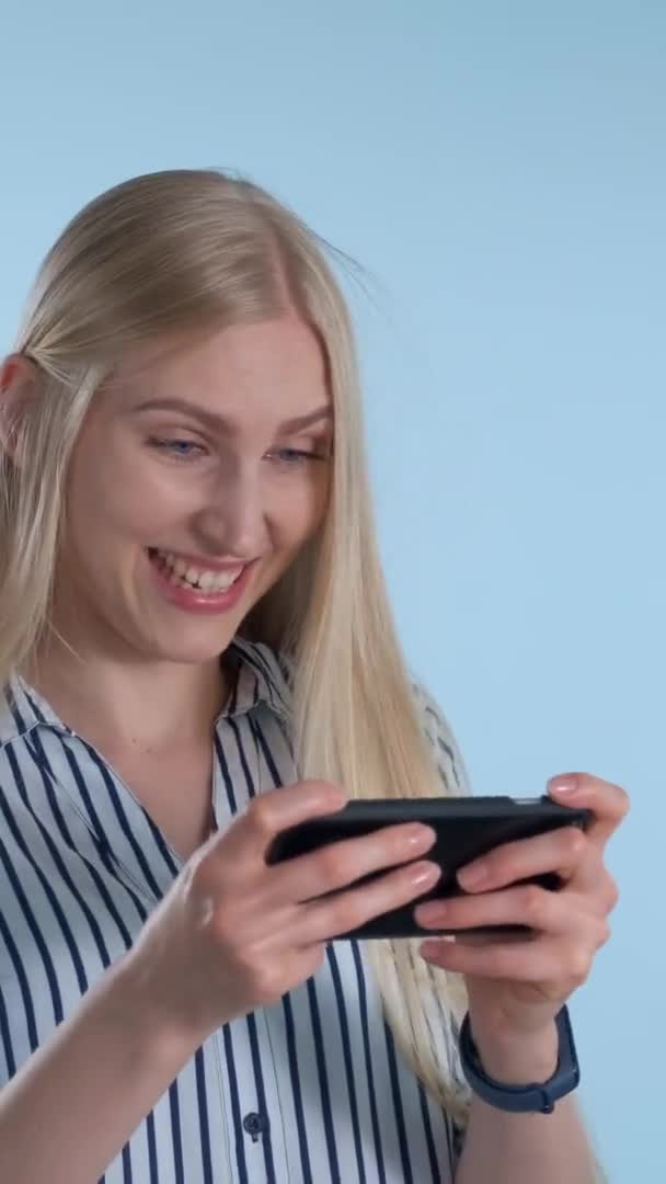 Красивая блондинка играет в игры на смартфоне на синем фоне — стоковое видео
