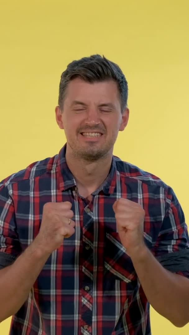 Homem animado em xadrez camisa levantando punhos em alegria no fundo amarelo . — Vídeo de Stock