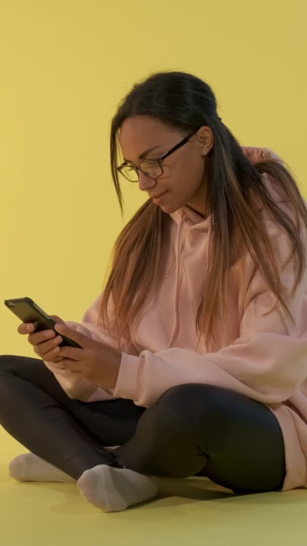 Wesoły czarny kobieta pisanie wiadomości na smartfon siedzi na podłodze. — Wideo stockowe