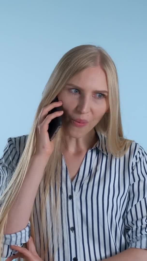 Angenehm aussehende junge Frau spricht mit jemandem per Smartphone auf blauem Hintergrund. — Stockvideo