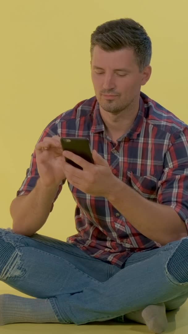Knappe jongen zit op de vloer en chatten met vrienden op de smartphone — Stockvideo