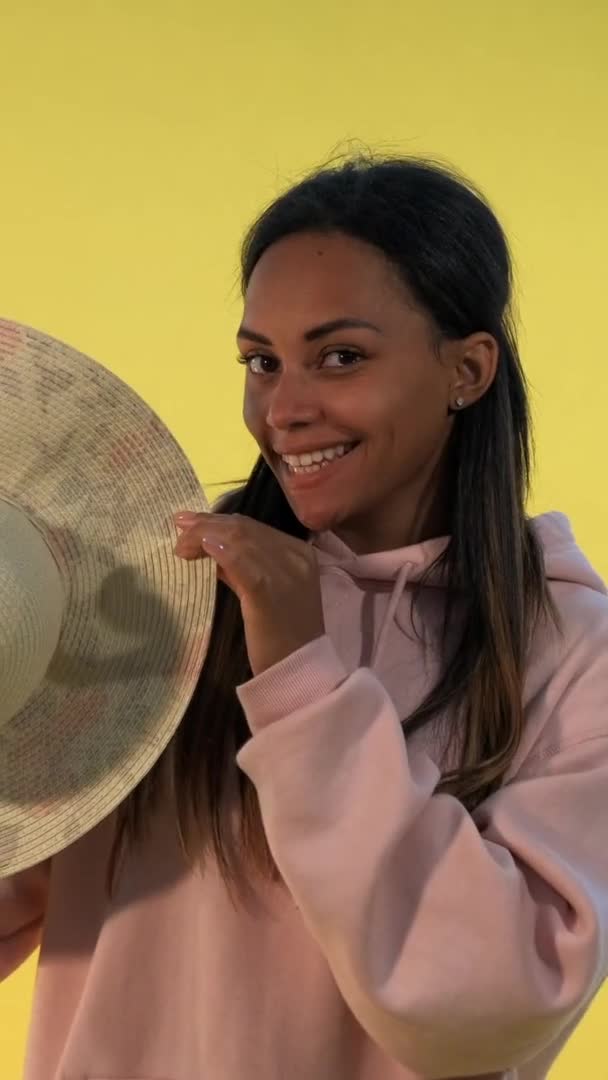 Glimlachende Afrikaanse vrouw verschuilen achter de hoed op gele achtergrond. — Stockvideo