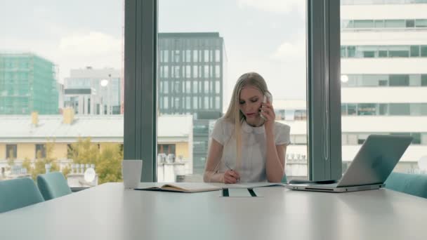 Femme sérieuse travaillant dans la salle de bureau de lumière. Élégante femme d'affaires moderne avec ordinateur portable et papiers à longue table dans la salle de conférence lumineuse ayant un appel téléphonique . — Video