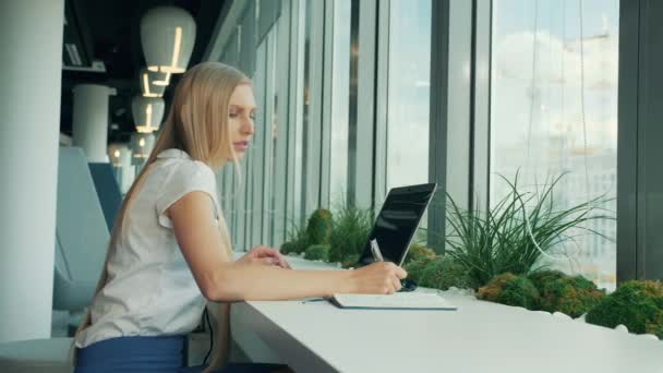 Τυπική γυναίκα με φορητό υπολογιστή και έγγραφα. Μερική άποψη του επιχειρηματίας γραψίματος σε χαρτί ενώ κάθεται με το laptop στο τραπέζι κοντά στο παράθυρο στο σύγχρονο γραφείο. — Αρχείο Βίντεο