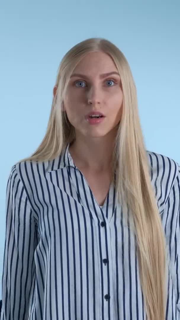 Jeune femme blonde étendant ses mains sur les côtés et disant "quoi" sur fond bleu . — Video