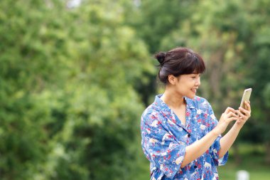 Onun smartphone okurken, mesaj yaz yazarak ya da bir parkta dinlenirken akıllı telefonda Sohbet gülümseyen genç güzel Asyalı kadın. 