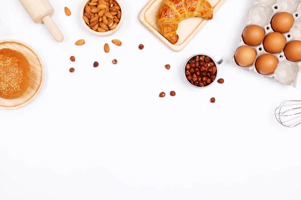 Homemade breads or bun, croissant and bakery ingredients, flour, almond nuts, hazelnuts, eggs on white background, Bakery background frame, Cooking breakfast concept. Flat lay, Top view and copy space