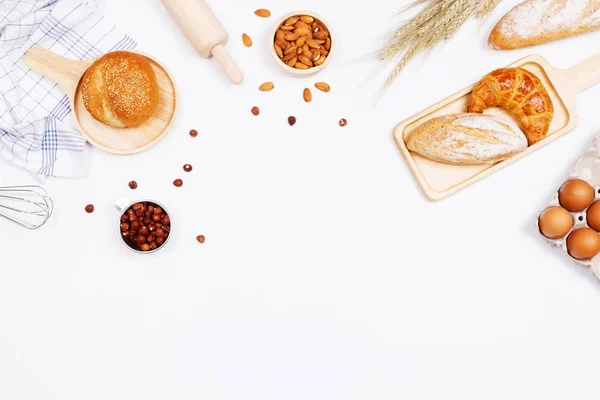 Homemade breads or bun, croissant and bakery ingredients, flour, almond nuts, hazelnuts, eggs on white background, Bakery background frame, Cooking breakfast concept. Flat lay, Top view and copy space