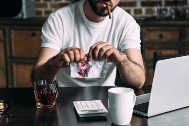 cropped shot of man smoking cigar and tearing photo of ex-girlfriend clipart