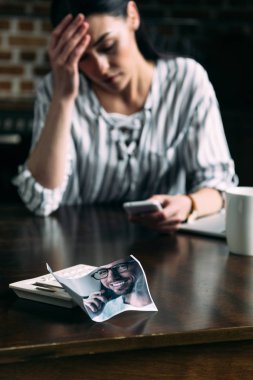young depressed woman using smartphone  with crumpled photo of ex-boyfriend on foreground