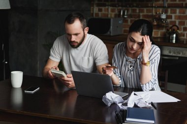 stressed young couple counting tax and bills with laptop and calculator clipart