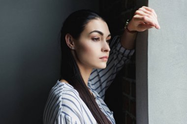 side view of depressed young woman leaning on wall and looking away clipart