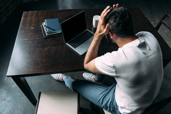 high angle view of tired freelancer remote working at table with laptop in kitchen at home