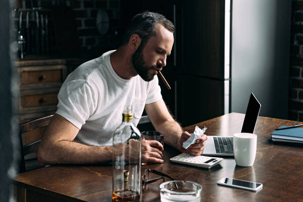 подавленный молодой человек курит сигару и смотрит на скомканное фото бывшей девушки
