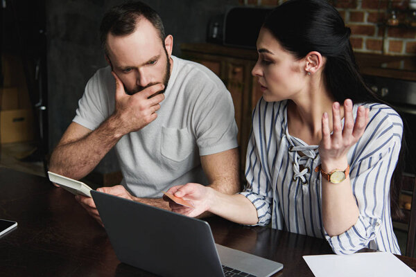 stressed young couple with laptop and calculator counting credit dept