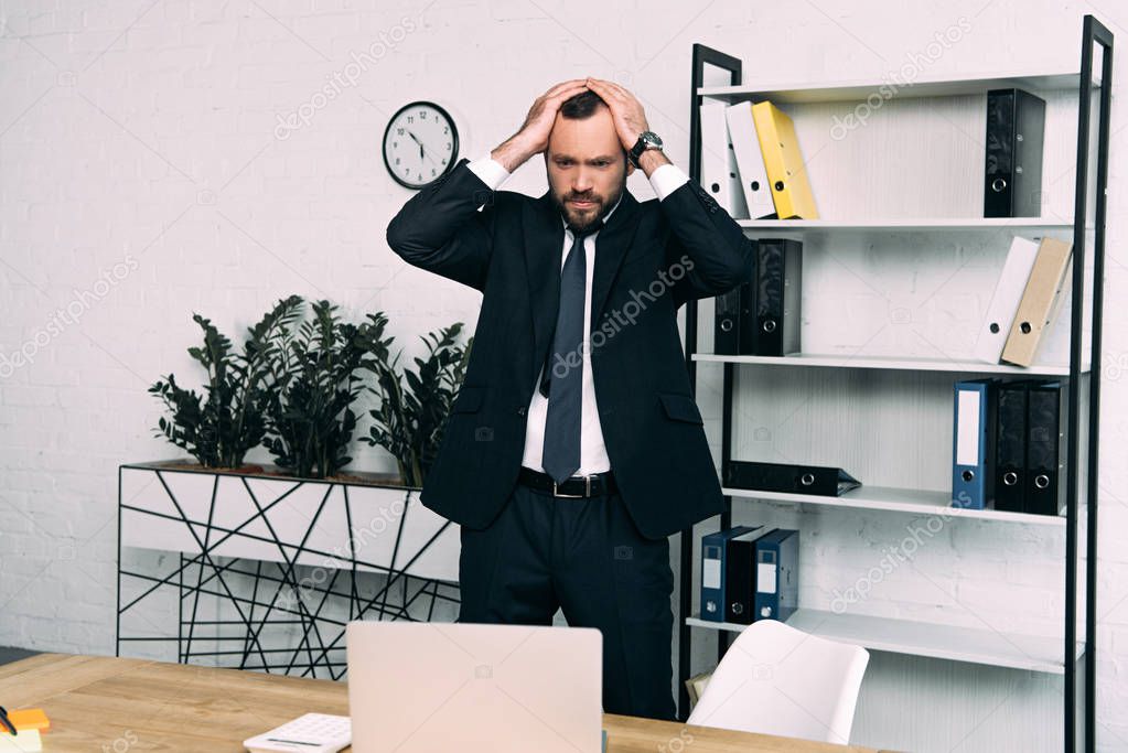 portrait of stressed businessman in suit standing at workplace in office