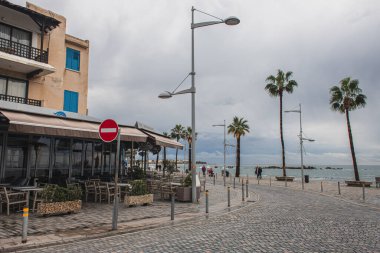 PAPHOS, CYPRUS - 31 Mart 2020: Bina yakınlarında yeşil palmiye ağaçları olan deniz kıyısı 