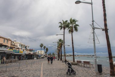 PAPHOS, CYPRUS - 31 Mart 2020: deniz kıyısındaki bebek arabası, insanlar ve palmiye ağaçları 