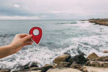 cropped view of woman holding red paper as location sign near mediterranean sea clipart