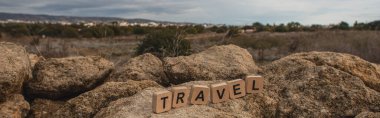 panoramic shot of wooden cubes with travel lettering on stones against sky clipart