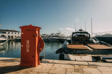 red booth with sos lettering near yachts in mediterranean sea clipart