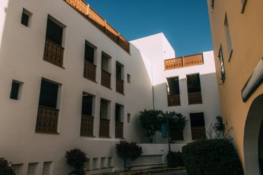 Mavi gökyüzüne karşı beyaz ve modern bina yakınında yeşil ağaçlar