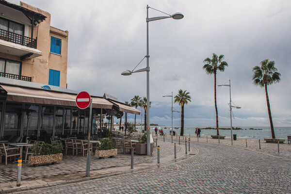 PAPHOS, CYPRUS - MARCH 31, 2020: sea shore with green palm trees near building 