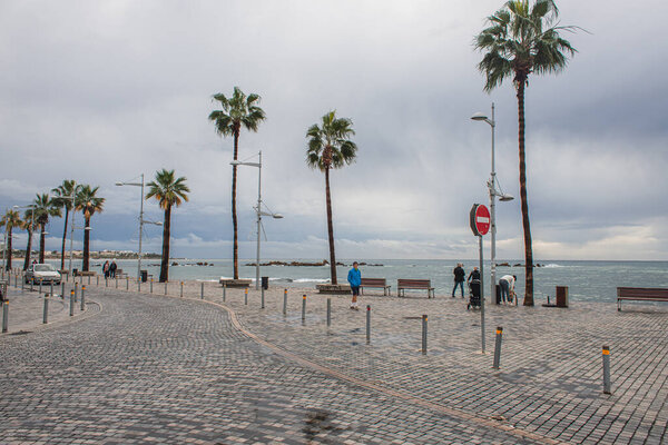 PAPHOS, CYPRUS - MARCH 31, 2020: sea shore with palm trees near people on street 