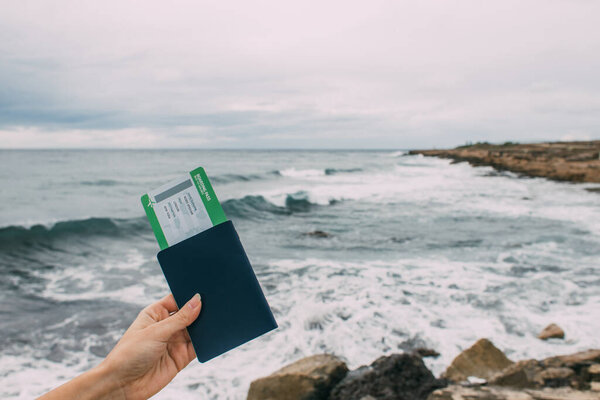 cropped view of woman holding passport with flight ticket near mediterranean sea 