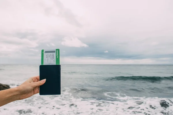 海の近くの航空券を持ってパスポートを保持する女性のクロップドビュー — ストック写真