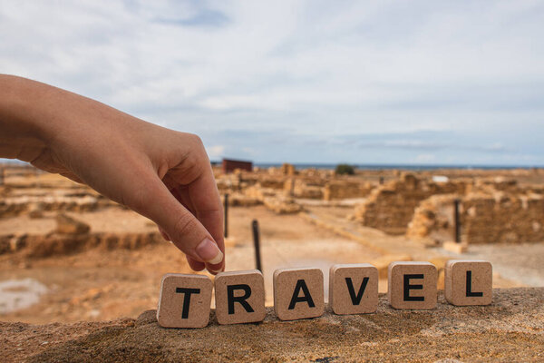 cropped view of woman touching wooden cubes with travel lettering near ruins of ancient House of Theseus  