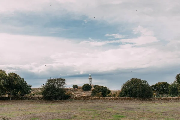 green trees and white lighthouse against blue sky with clouds 